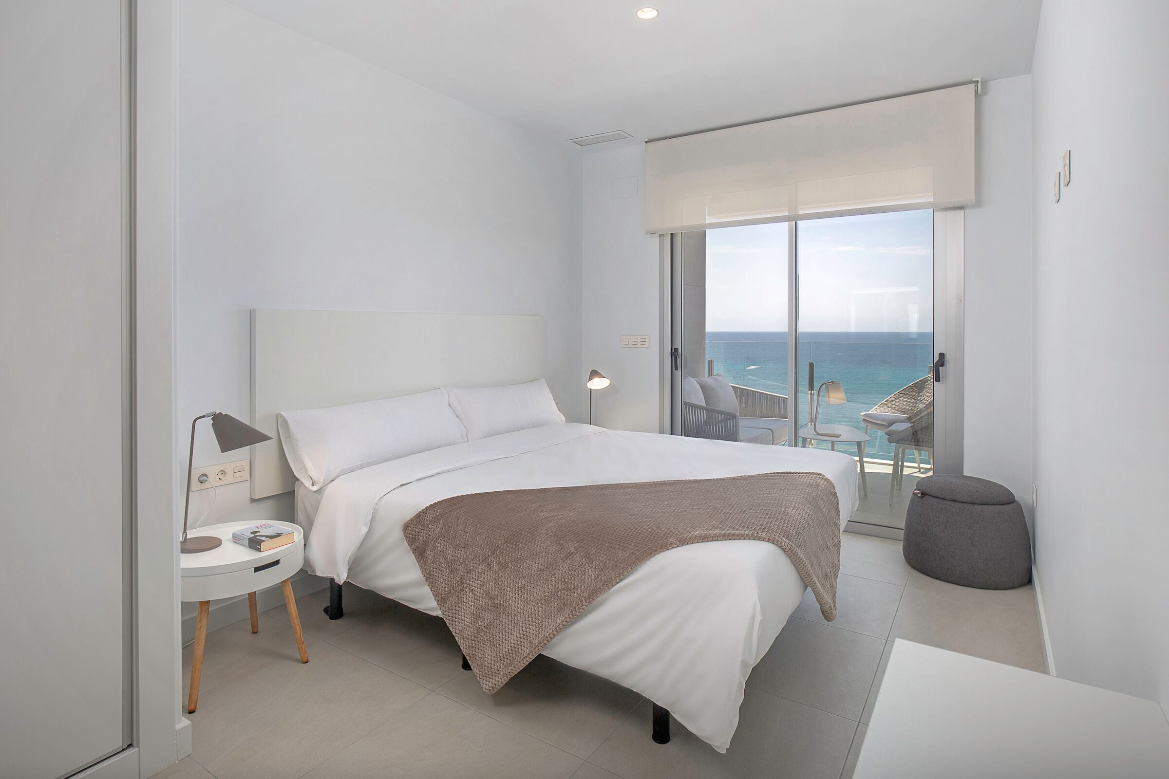 Ein modernes Schlafzimmer mit einem großen Bett, einem Nachttisch mit Lampe und Meerblick vom Balkon.