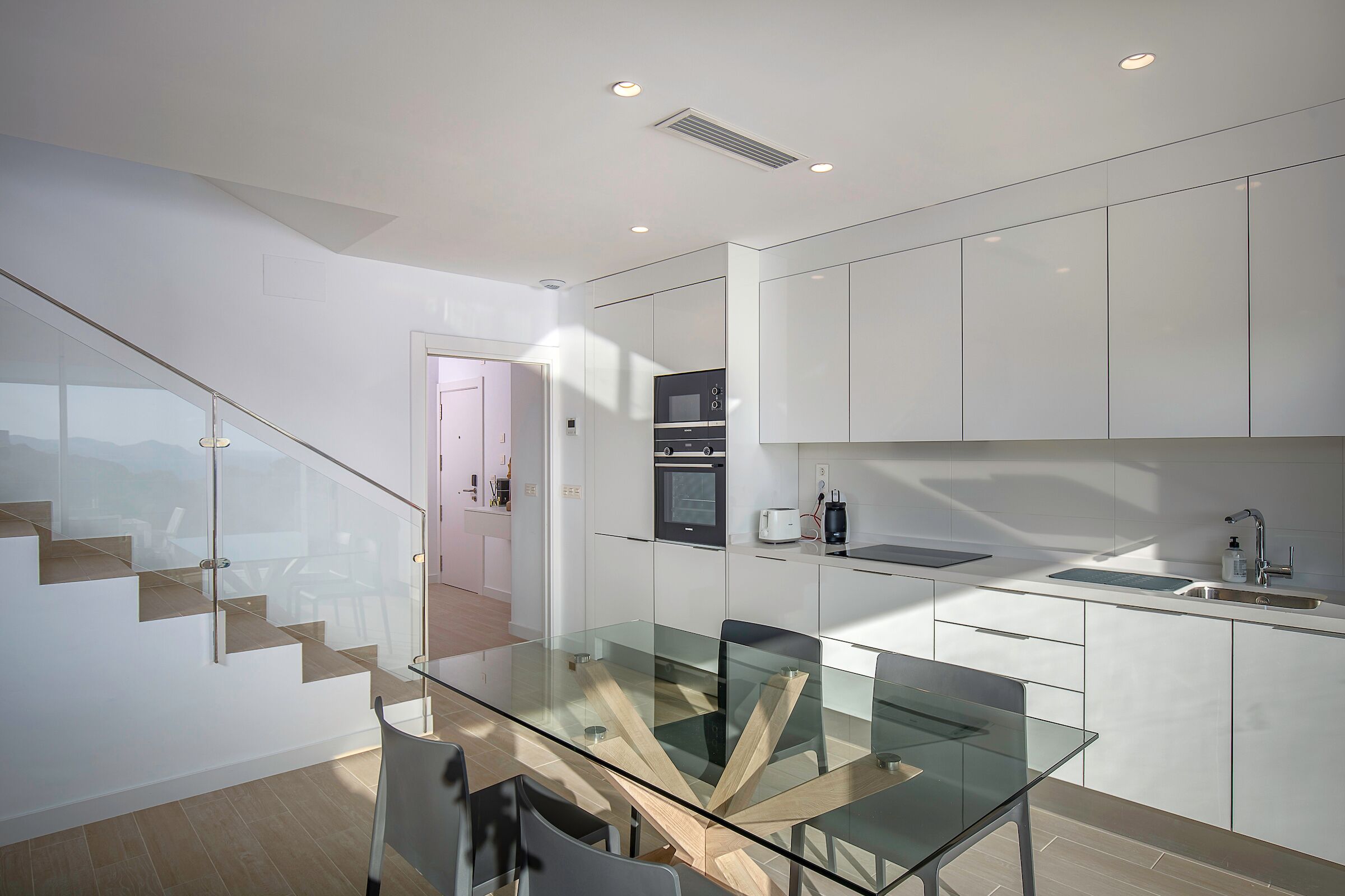 A modern kitchen with white cabinetry, a glass dining table, and a built-in oven.