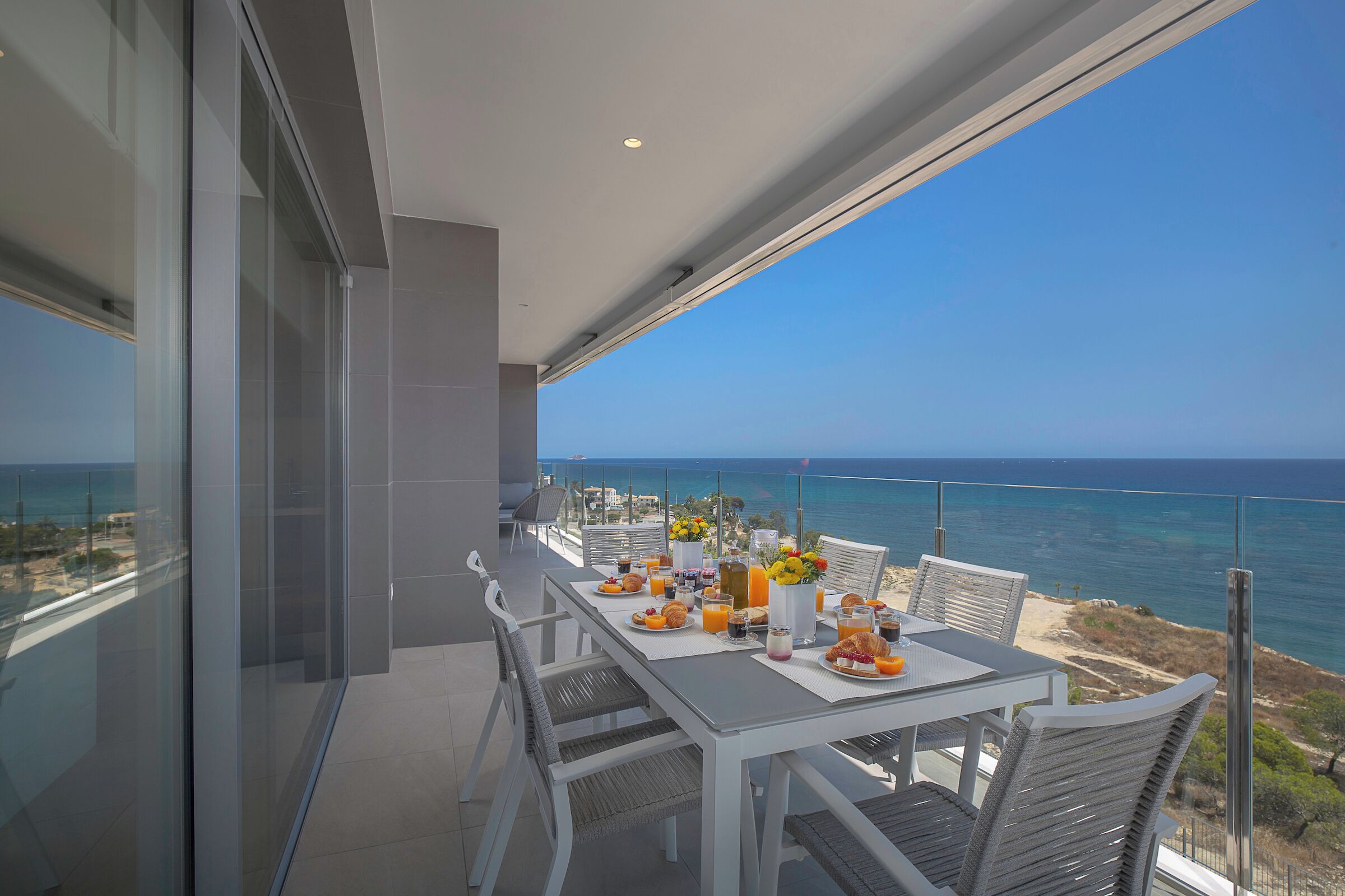 A balcony with a table set for breakfast overlooking the sea.