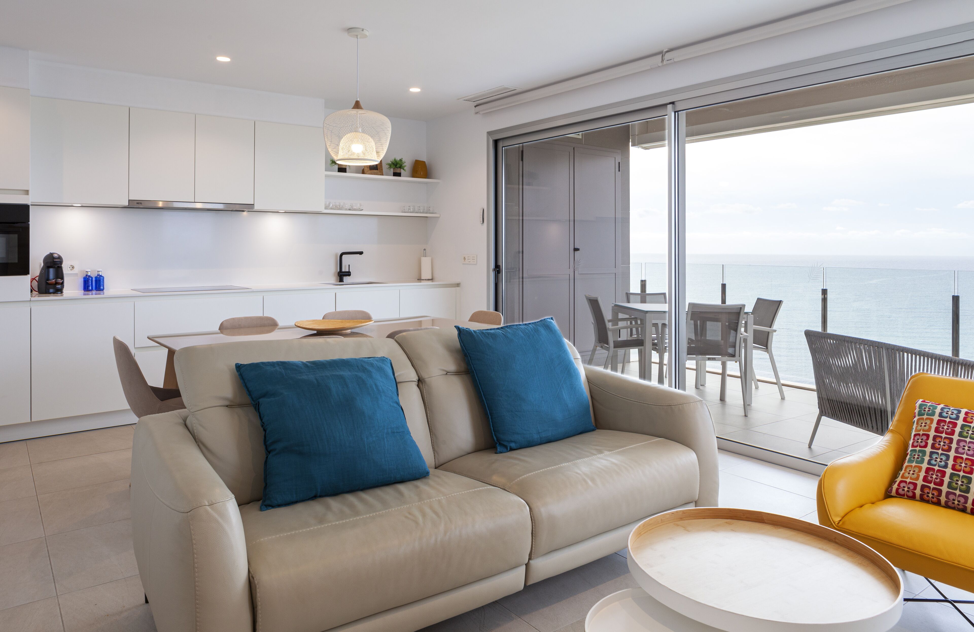 A modern living room with a beige sofa, a yellow armchair, and a dining area with a table and chairs.
