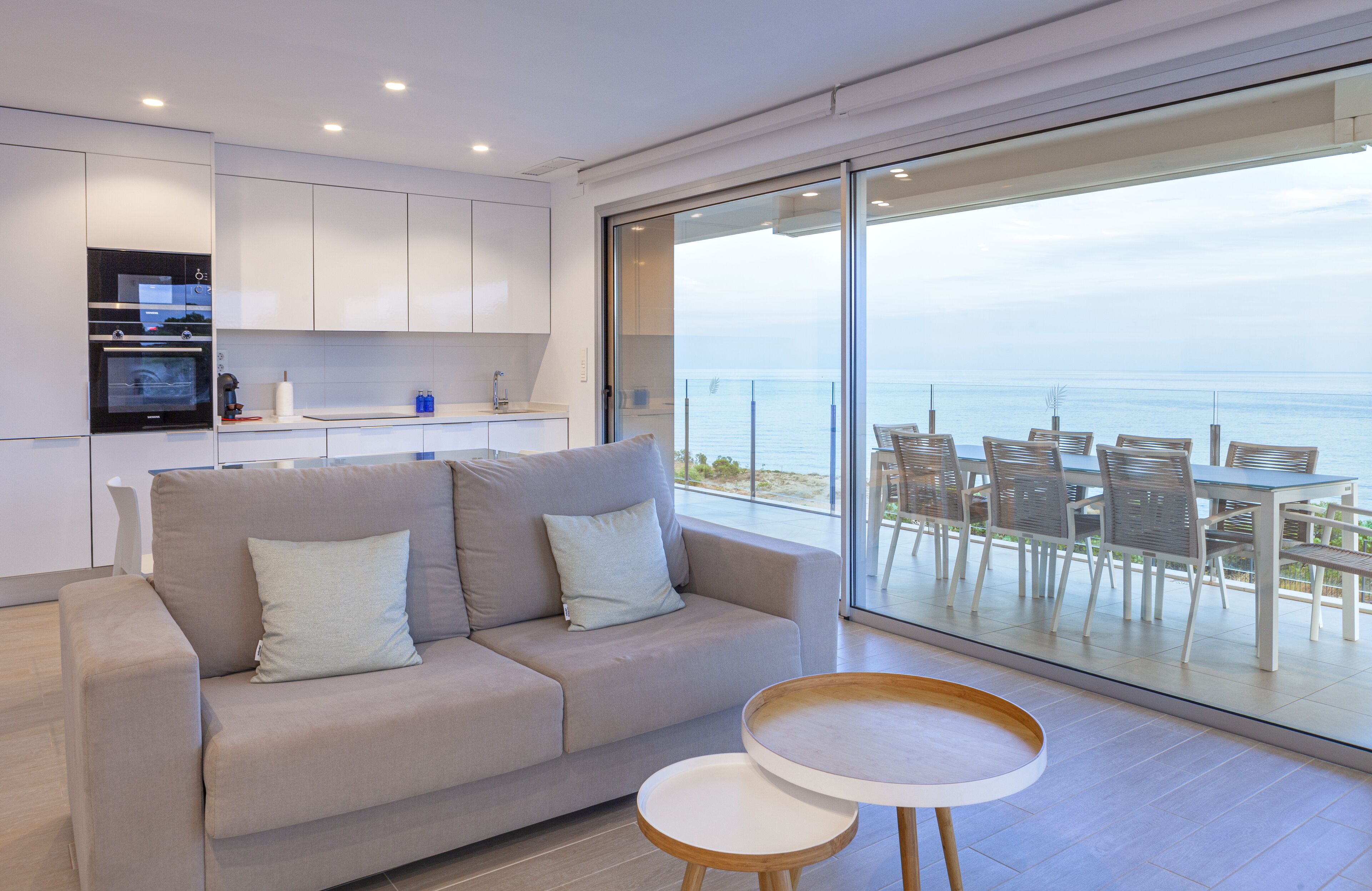 A modern living room with a sofa, a small round table, and a balcony with a view of the sea.