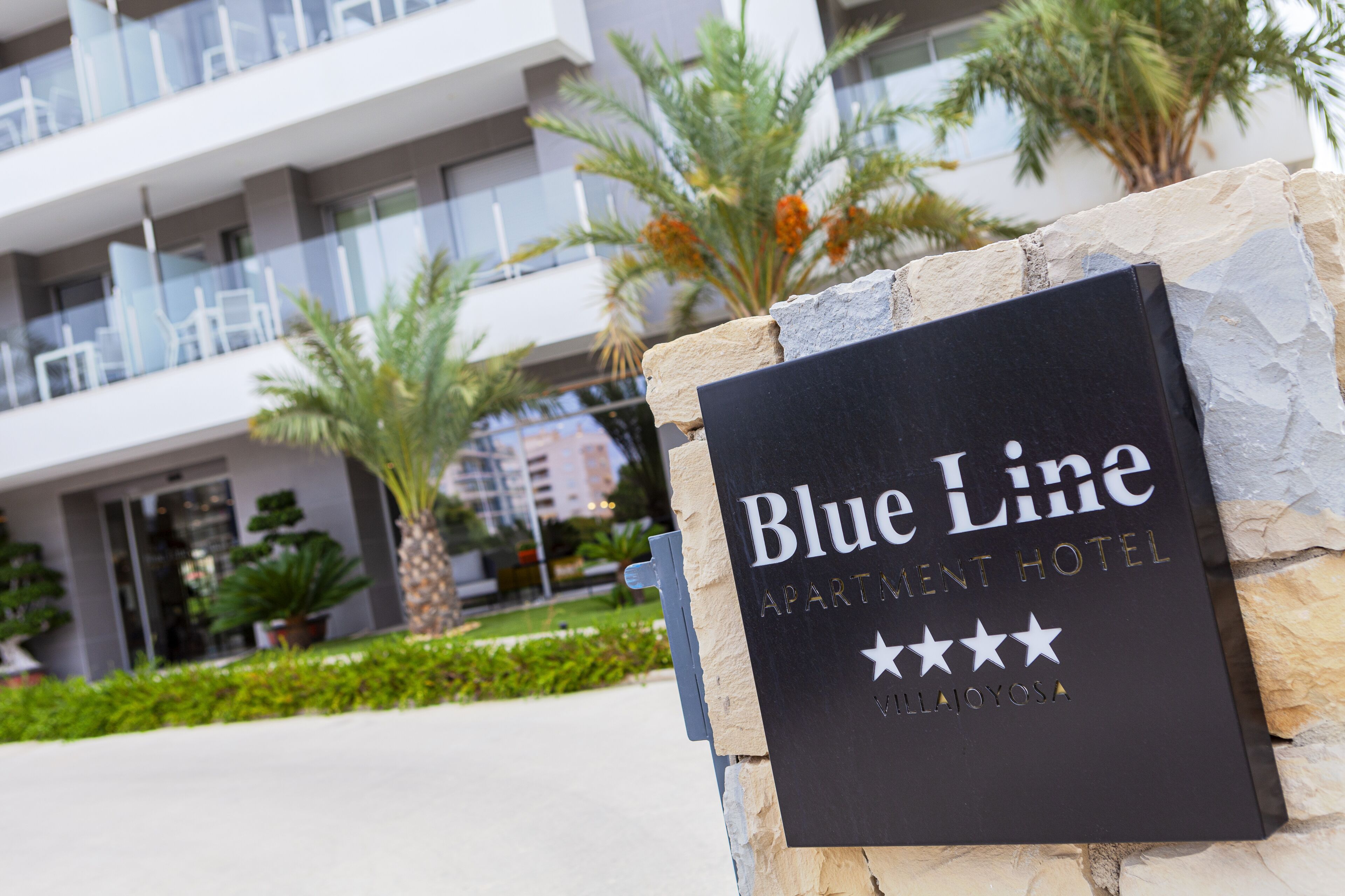 Ein Schild für das Blue Line Apartment Hotel mit einem modernen Gebäude im Hintergrund.