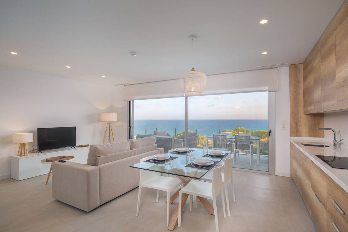 Ein modernes Wohnzimmer mit einem Glastisch, einer Couch, einem Fernseher und Meerblick.
