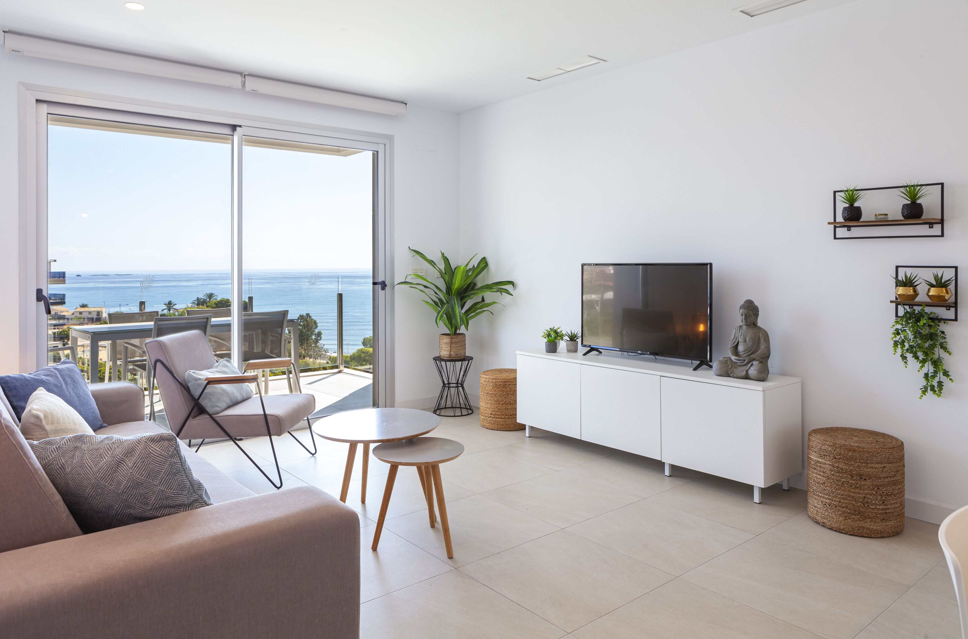 Un salon moderne doté d’un grand téléviseur, de sièges confortables, d’un balcon avec vue sur la mer et d’une décoration minimaliste.