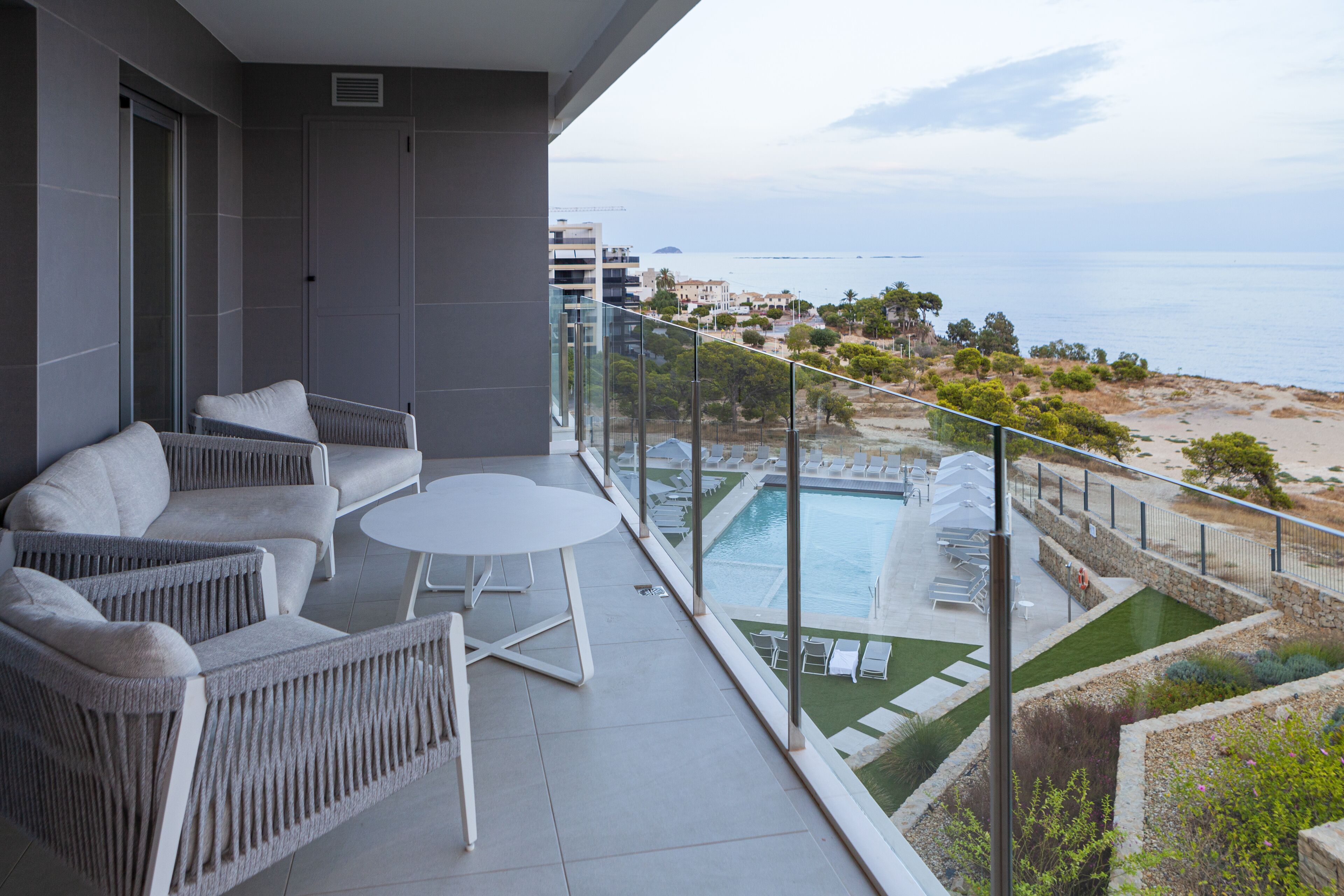 Un balcón con mobiliario de mimbre, piscina y vistas a la playa y al océano.