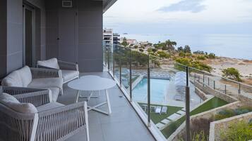 Un balcón con mobiliario de mimbre, piscina y vistas a la playa y al océano.