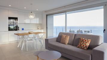 Una cocina moderna con armarios blancos, un comedor con mesa y sillas de madera, y un sofá gris con cojines estampados.