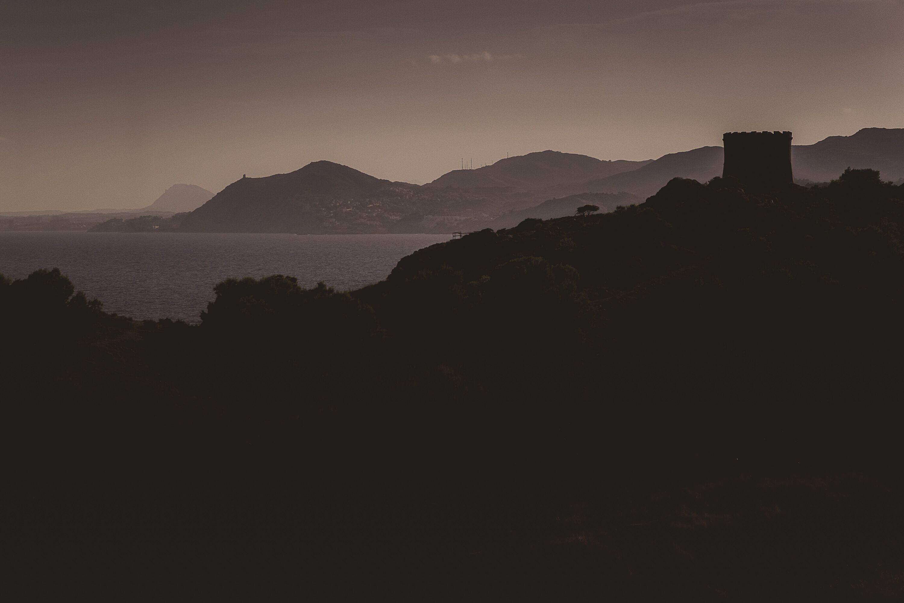 A coastal landscape with a prominent tower structure on a hill, overlooking a body of water.