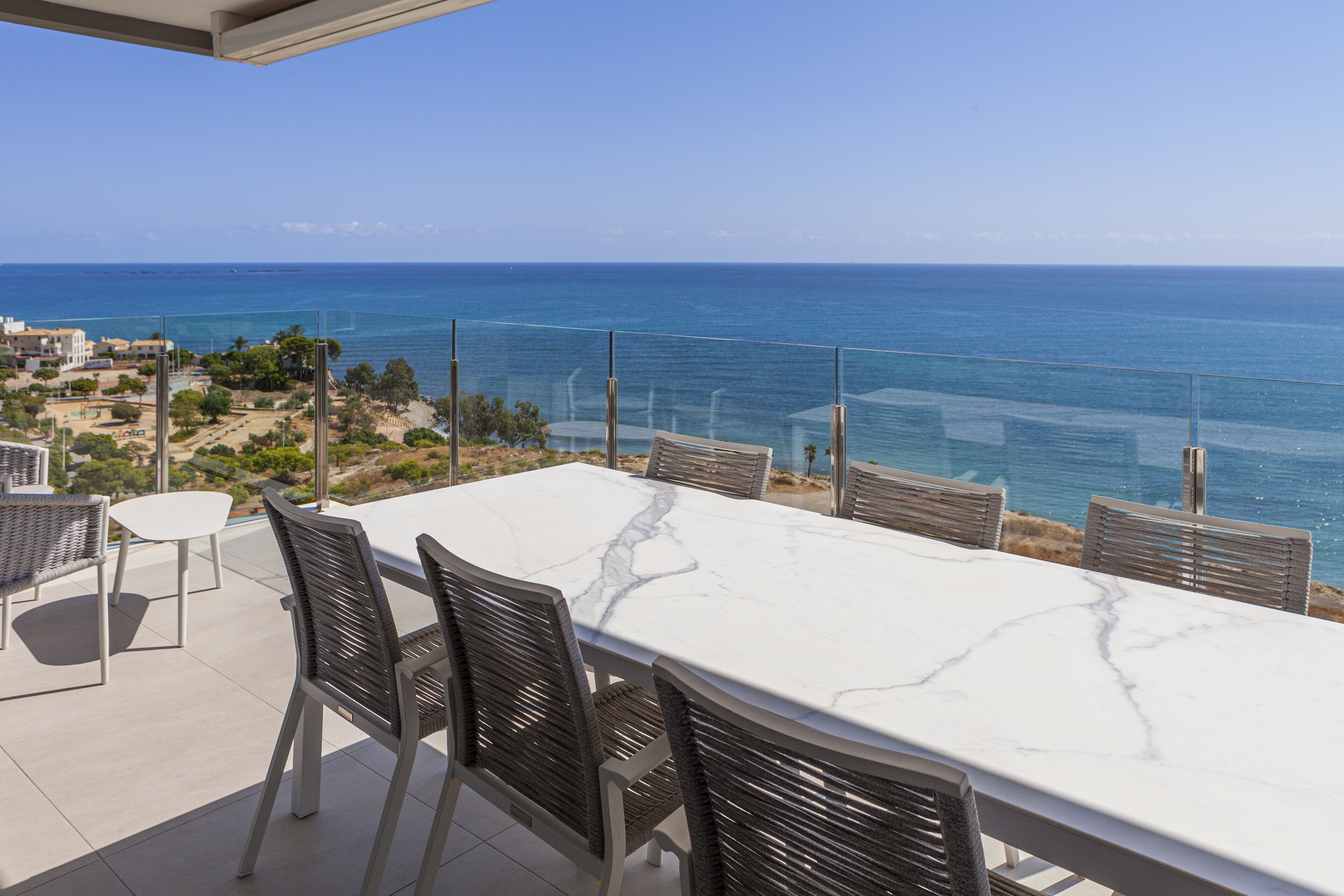 Eine Terrasse mit einem weißen Marmor-Tisch und Korbstühlen, mit Blick auf die Küste.