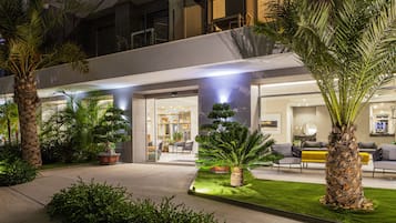 Un moderno vestíbulo de hotel con entrada de vidrio, plantas de interior y una zona de estar.