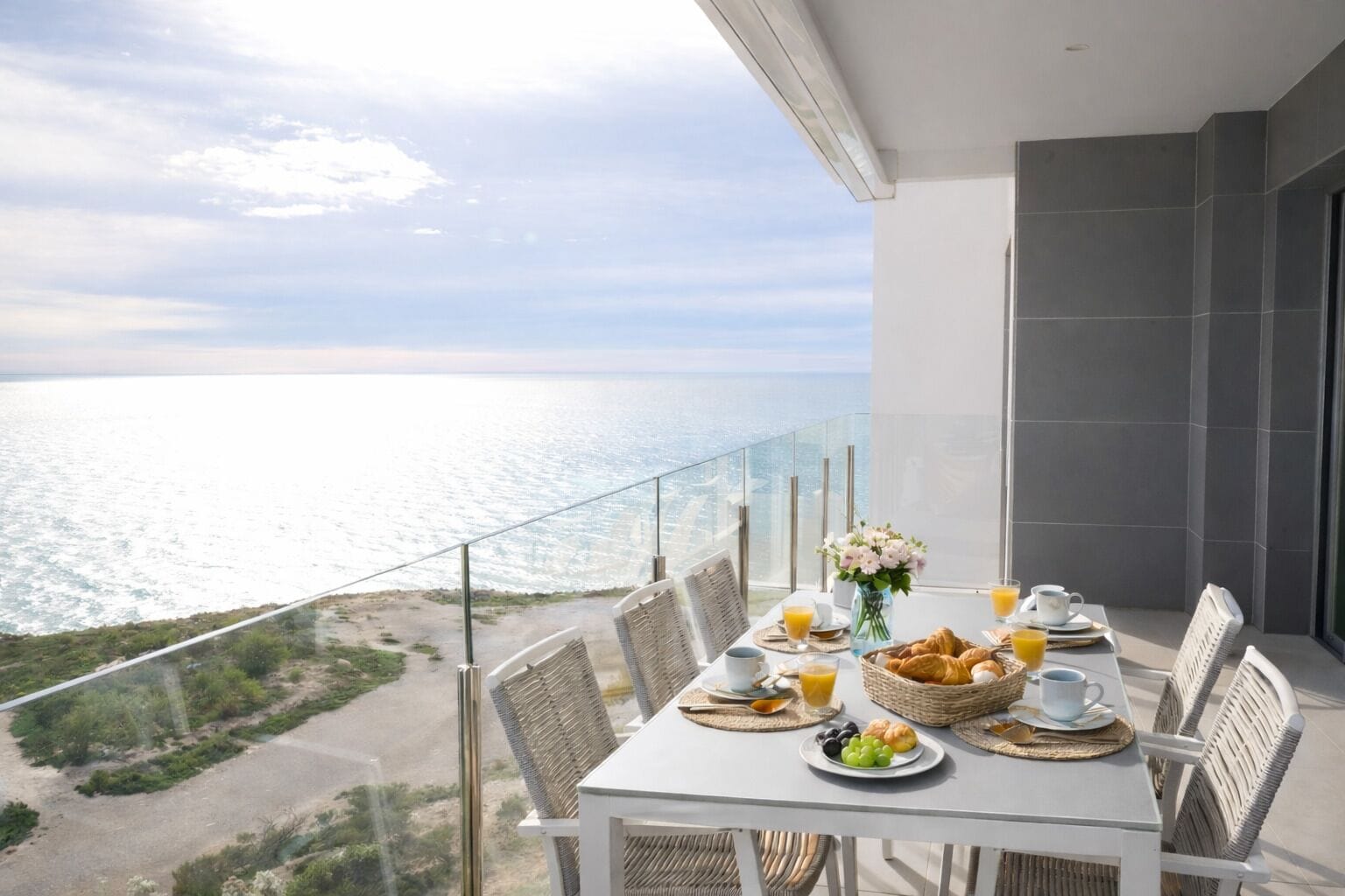 Un balcón con una mesa dispuesta para el desayuno, con vistas a la costa.