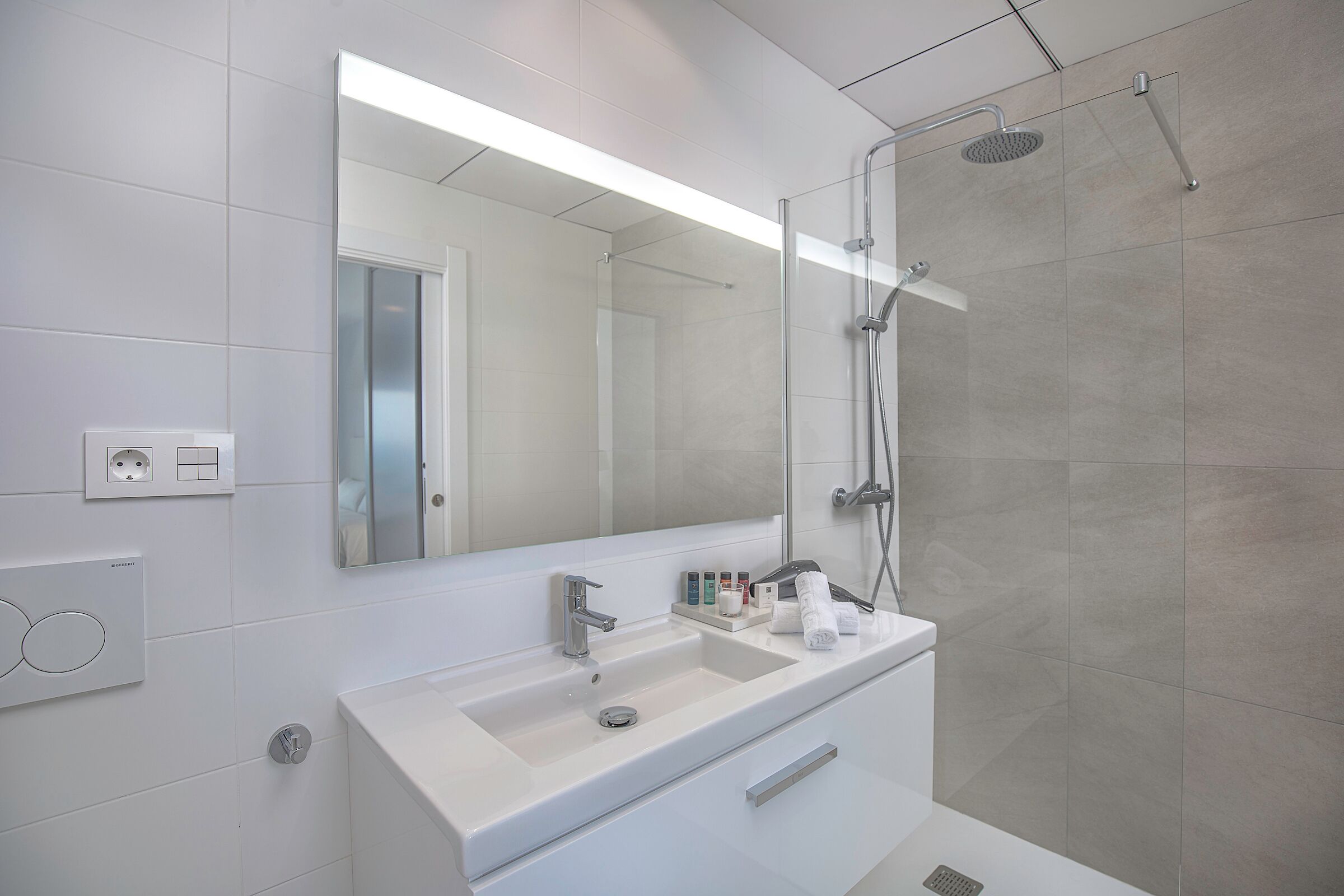 A modern bathroom with a large mirror, a white sink, and a glass-enclosed shower.