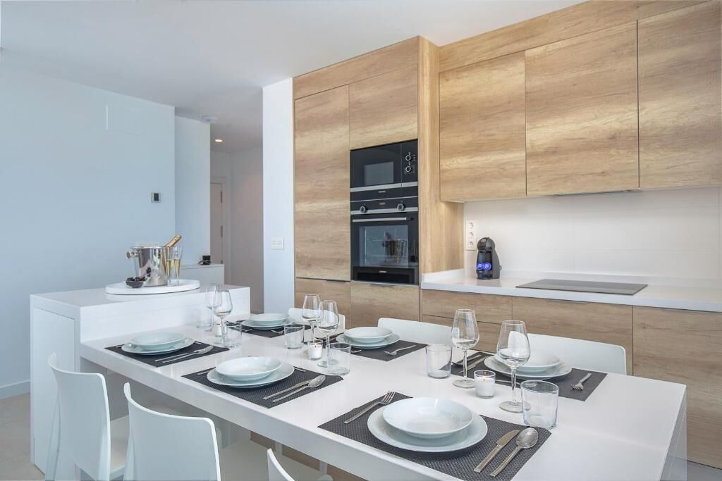 Una cucina moderna con mobili in legno, forno integrato e zona pranzo per sei persone, con sedie bianche e un tavolo lungo.