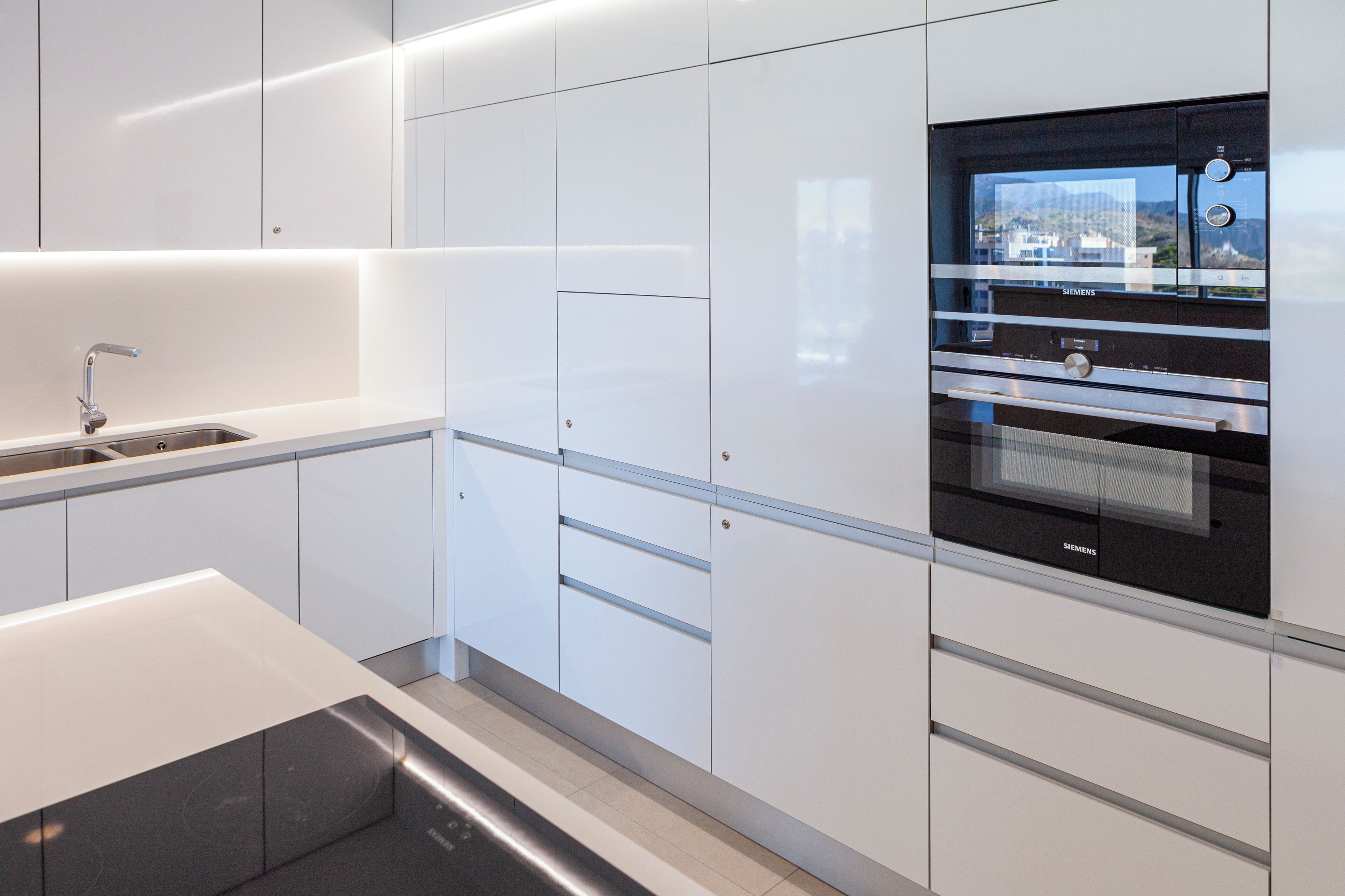 Una cocina moderna con armarios blancos, un lavamanos de acero inoxidable y un horno empotrado.