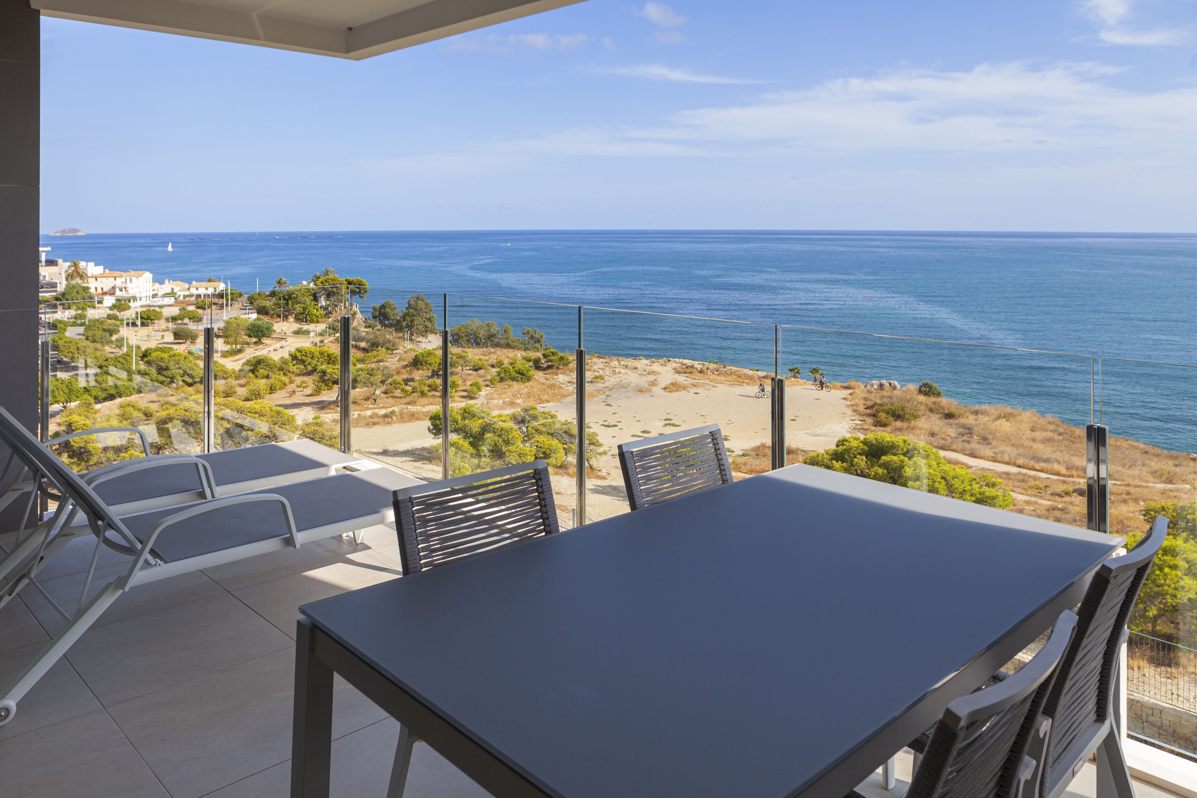 Un balcón con mesa y sillas, con vista a una playa y al mar.