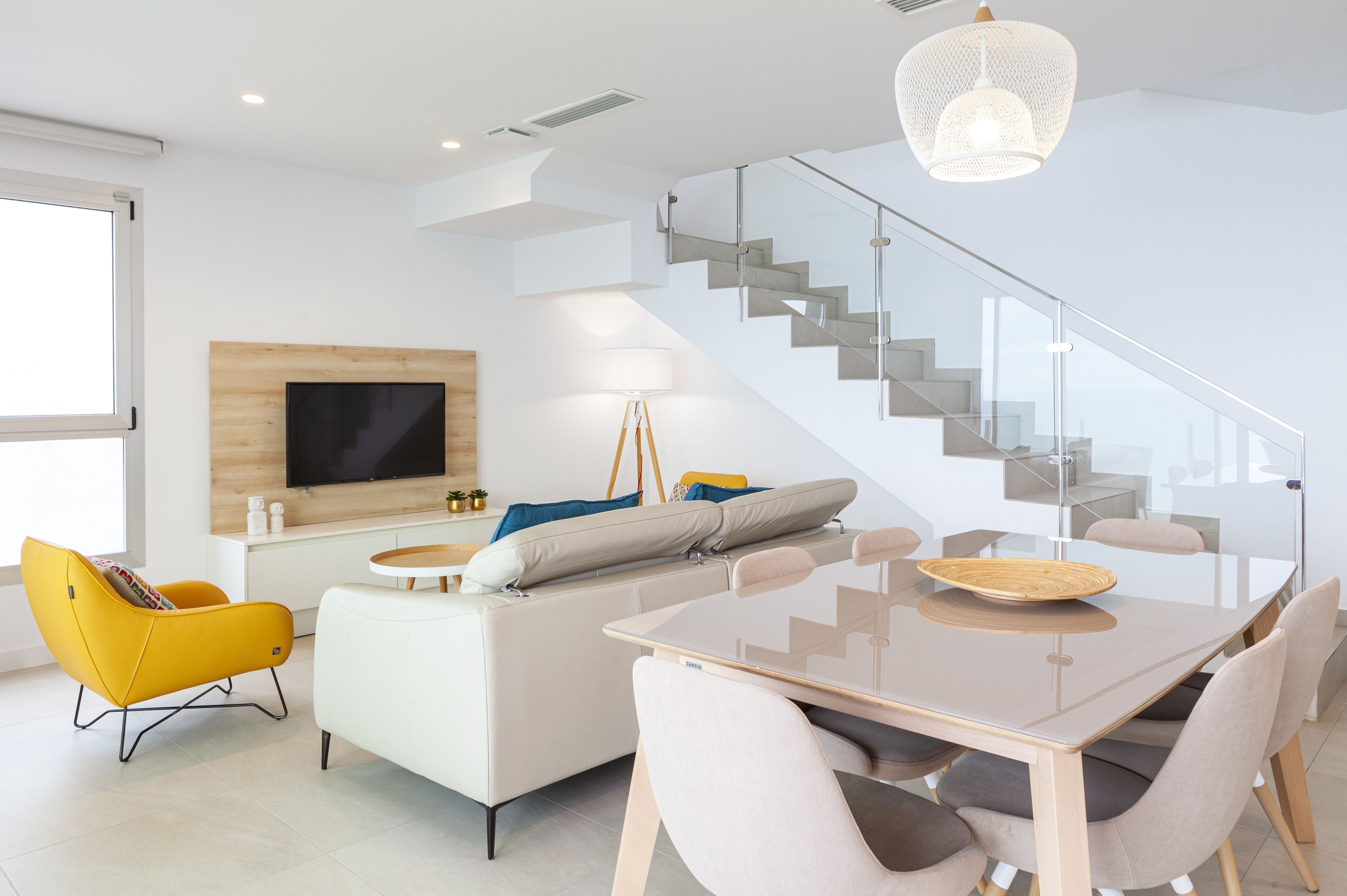 A modern living room with a sofa, yellow armchair, and a dining table with chairs.