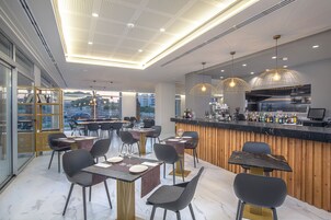 Restaurante moderno com área de bar, piso de mármore e mobiliário contemporâneo.