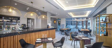 A modern restaurant with a bar area, wooden accents, and contemporary lighting fixtures.