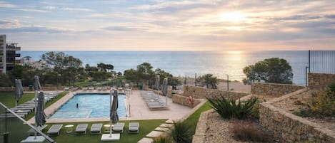Zona de piscina con sillones de descanso, pared de piedra y vista al mar.