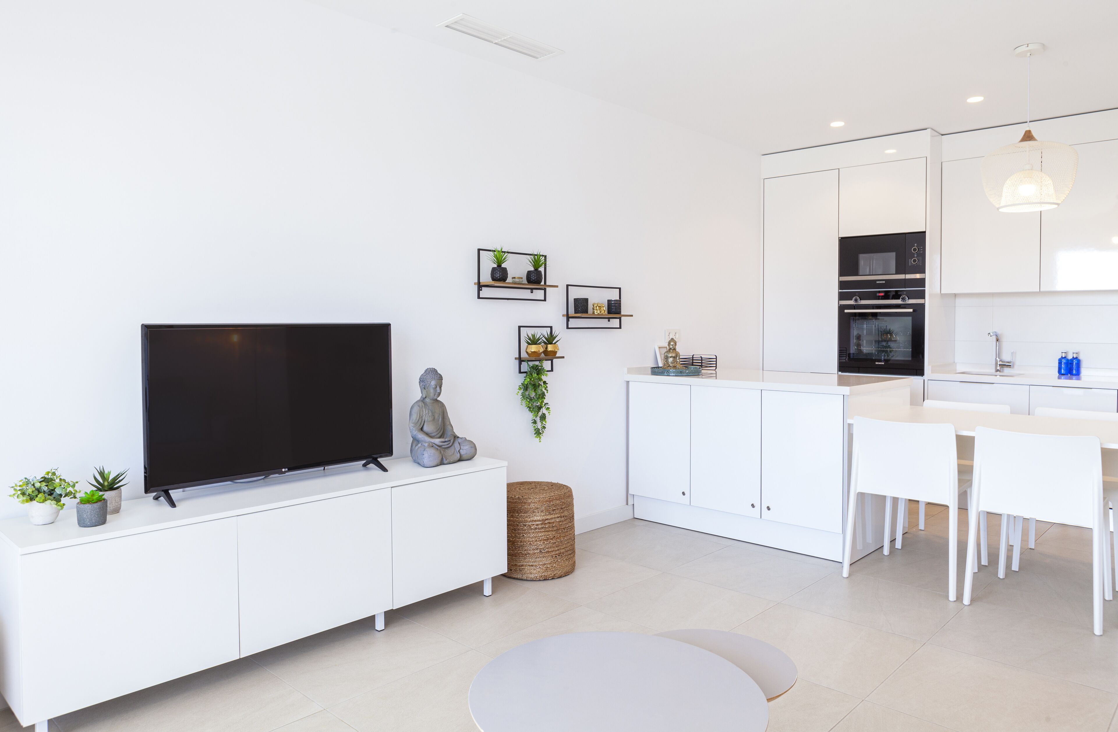 A modern kitchen with white cabinets, a built-in oven, and a dining area with white chairs.