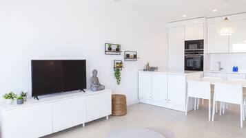 A modern kitchen with white cabinets, a built-in oven, and a dining area with white chairs.