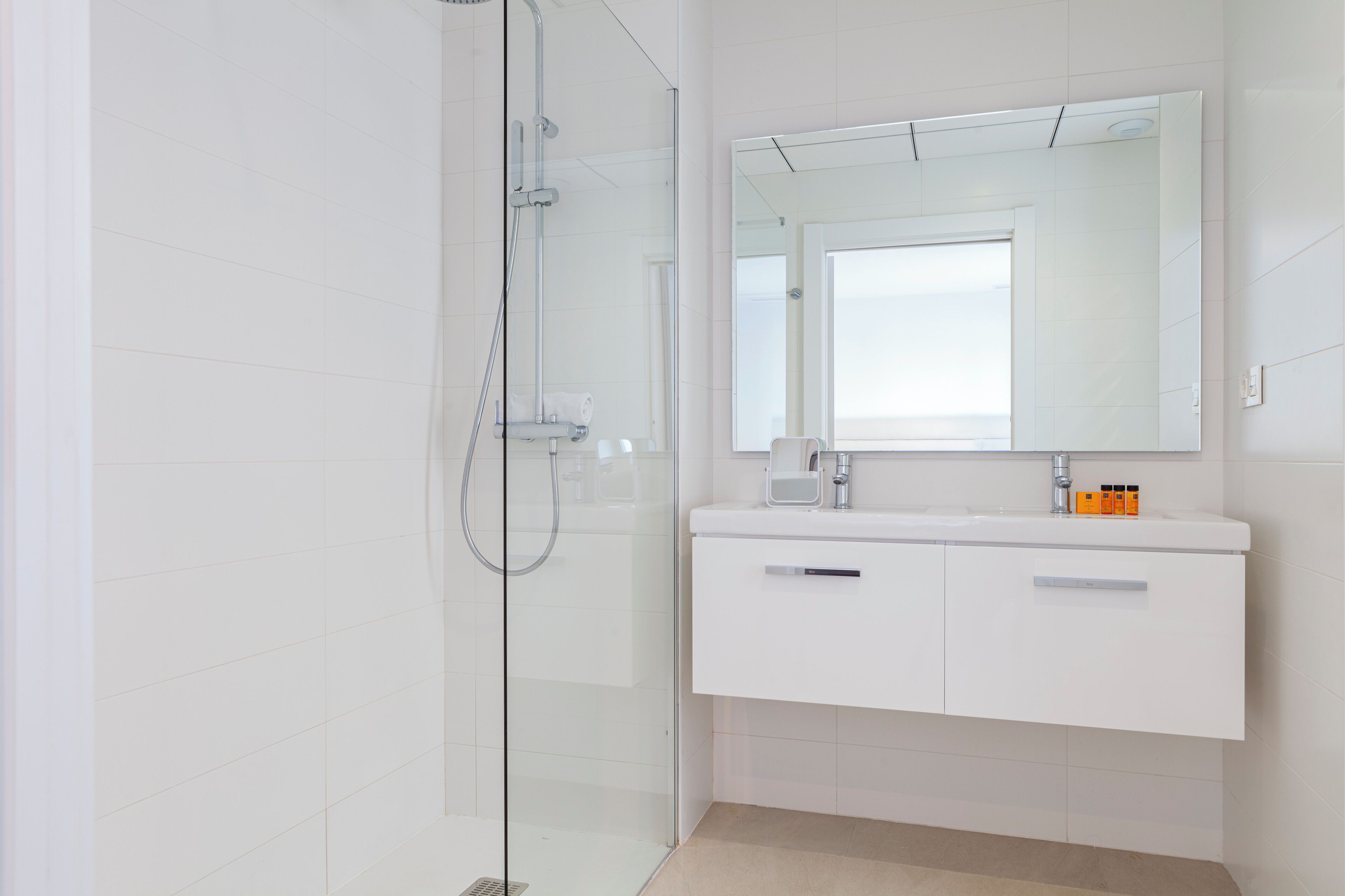 A modern bathroom with a glass shower enclosure, a white vanity with a mirror, and a sink.