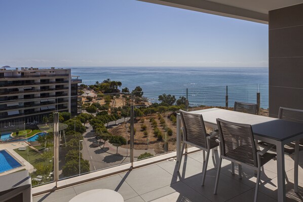 A balcony with a view of the sea, a pool, and a building complex.