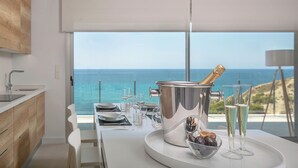 Een moderne keuken met uitzicht op zee, een eettafel gedekt met glazen en een champagnefles, plus een schaal fruit.