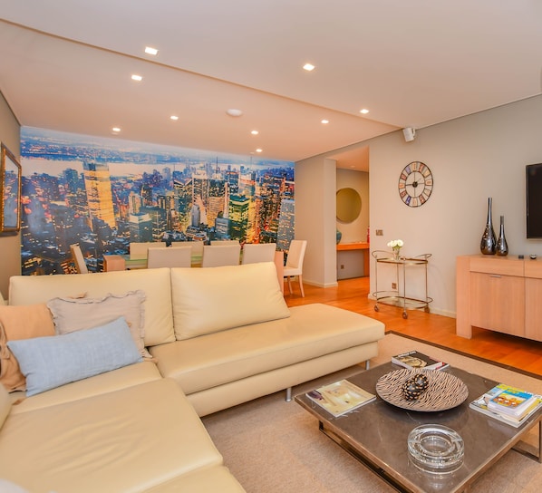 A modern living room with a sofa, coffee table, TV, and a cityscape mural.
