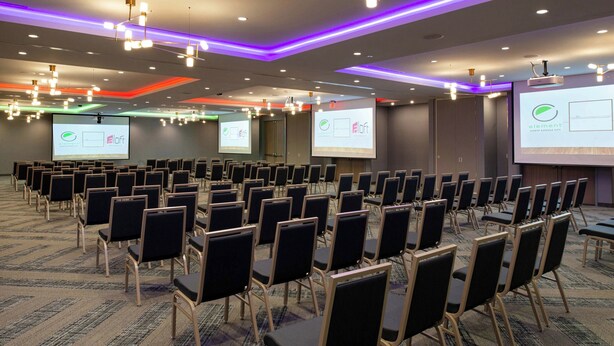 A conference room with rows of chairs, a projector screen, and presentation slides. - Aloft by Marriott North Kansas City (North Kansas City)