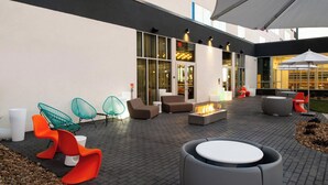 An outdoor seating area with modern furniture, a fire feature, and a large umbrella. - Aloft by Marriott North Kansas City (North Kansas City)