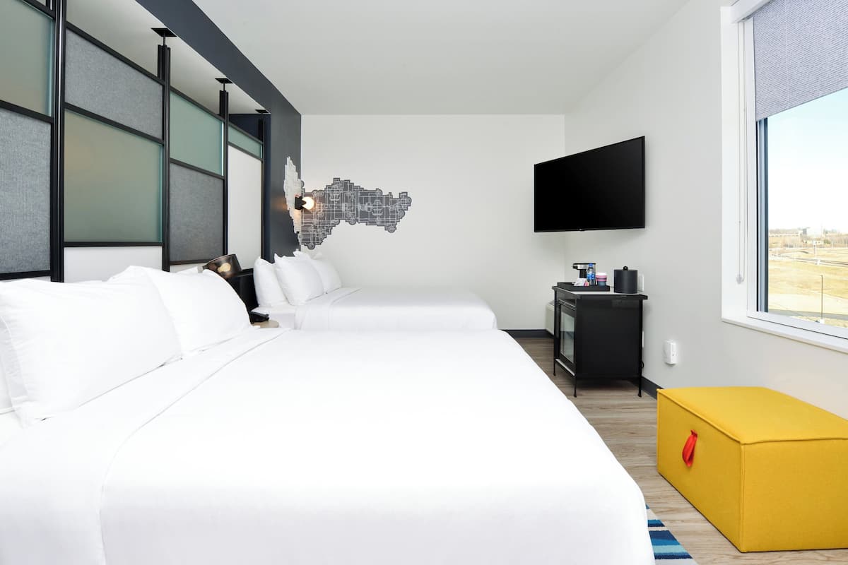 A hotel room with two beds, a flat-screen TV, a map artwork on the wall, and a window with a view.