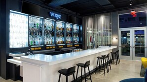 A bar area with a white countertop, black bar stools, and a neon sign above the bar. - Aloft by Marriott North Kansas City (North Kansas City)
