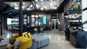 A modern lobby with seating areas, a reception desk, and a large digital screen. - Aloft by Marriott North Kansas City (North Kansas City)