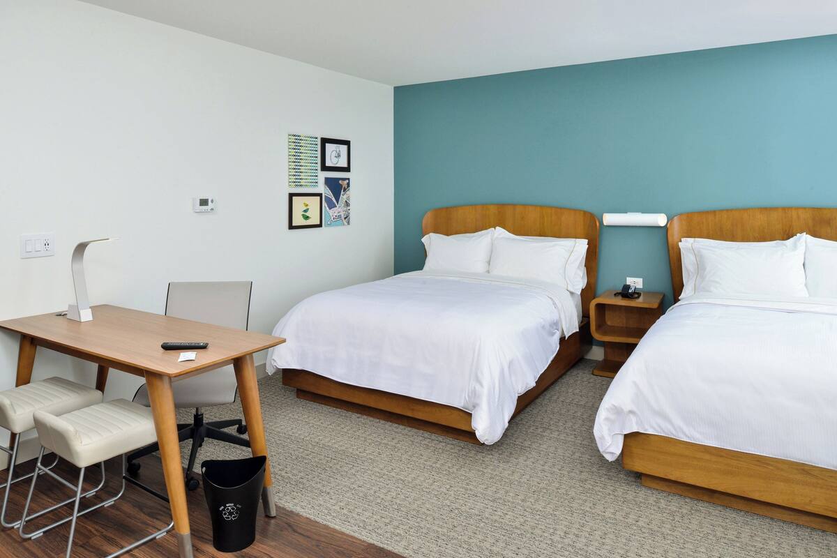 A hotel room with two beds, a desk, and a chair.