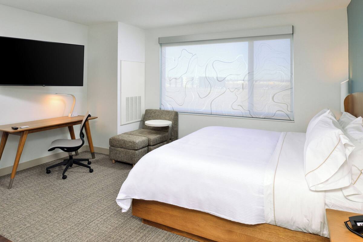 A hotel room with a bed, a desk, a chair, a television, and a window with a view.