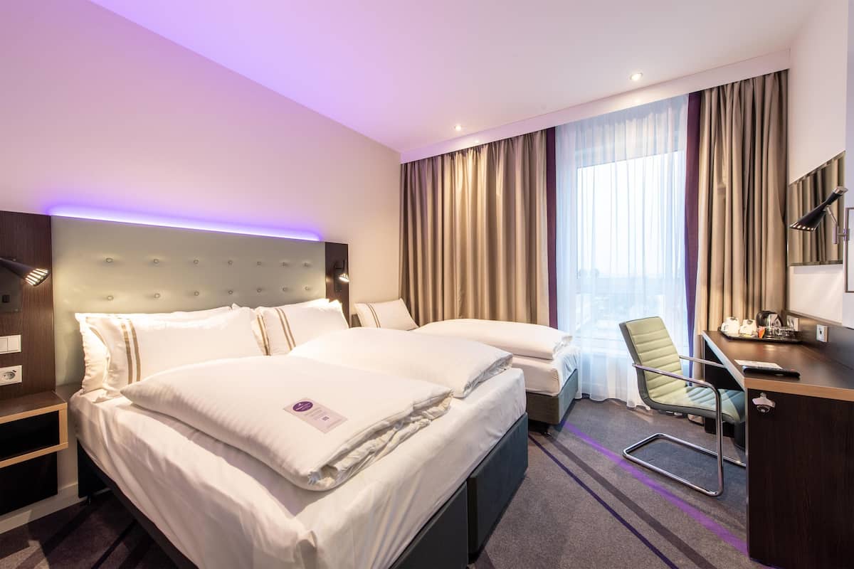 Habitación de hotel con dos camas, un escritorio, una silla, una lámpara y vistas a la ciudad.