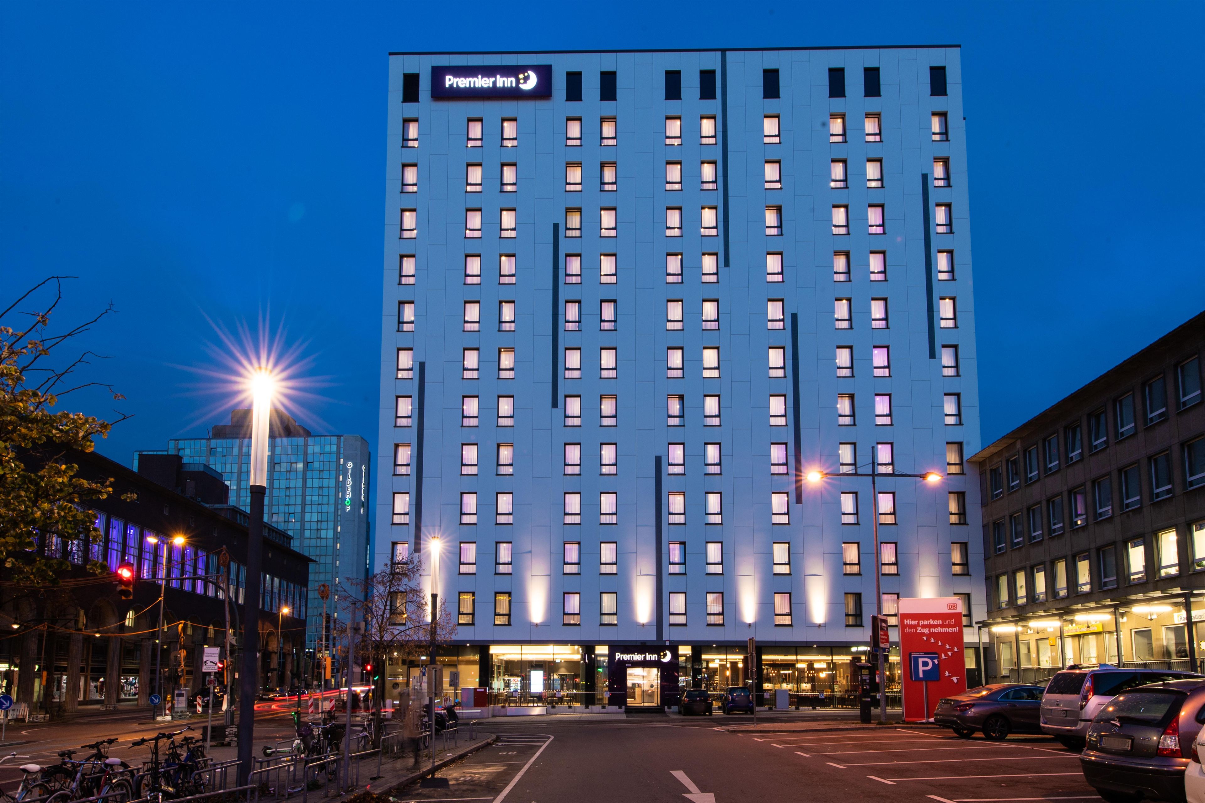 A tall hotel building with a prominent 'Premier Inn' sign, multiple floors, and a parking area in front.