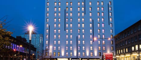 A tall hotel building with a prominent 'Premier Inn' sign, multiple floors, and a parking area in front.