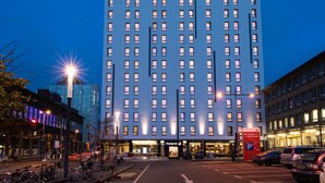 Un edificio de hotel alto con un llamativo letrero de 'Premier Inn', varios pisos y un estacionamiento al frente.
