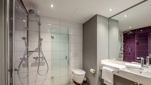 Un baño moderno con ducha envuelta en vidrio, inodoro y lavamanos con espejo.