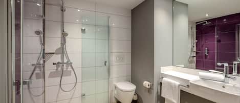 Un baño moderno con ducha envuelta en vidrio, inodoro y lavamanos con espejo.