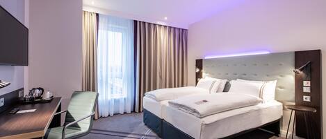 A hotel room with a bed, a desk, a chair, a TV, and a window with curtains.