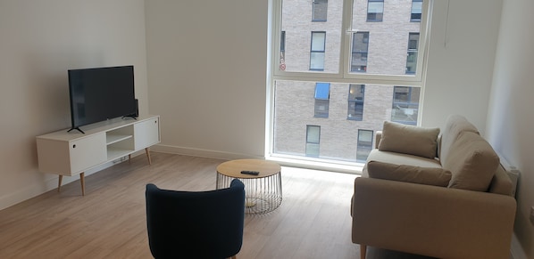 A modern living room with a flat-screen TV on a white cabinet, a round coffee table, a black chair, and a beige sofa. - Quay Apartments Exchange Quay (Salford)