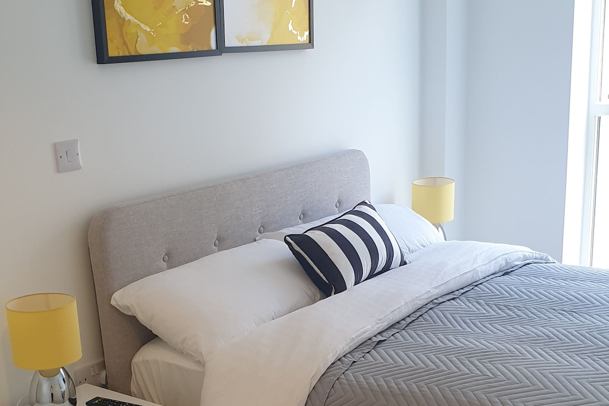Un dormitorio con cama, mesita de noche, lámpara y arte abstracto en la pared.