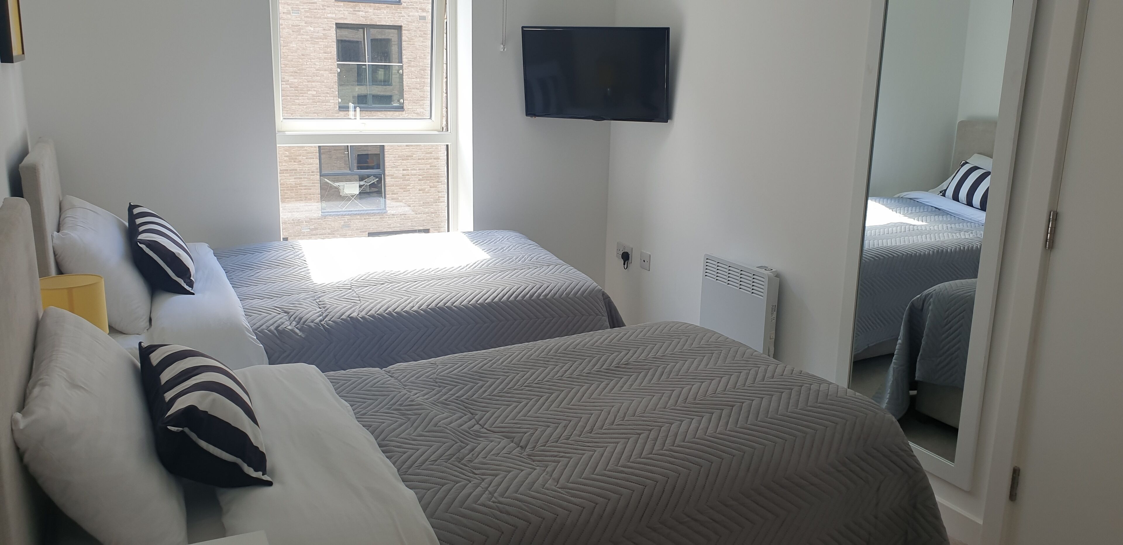 A hotel room with two beds, a TV mounted on the wall, and a window with a view of a building.