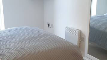 A bedroom with a bed, a TV mounted on the wall, a radiator, and a window with a view.