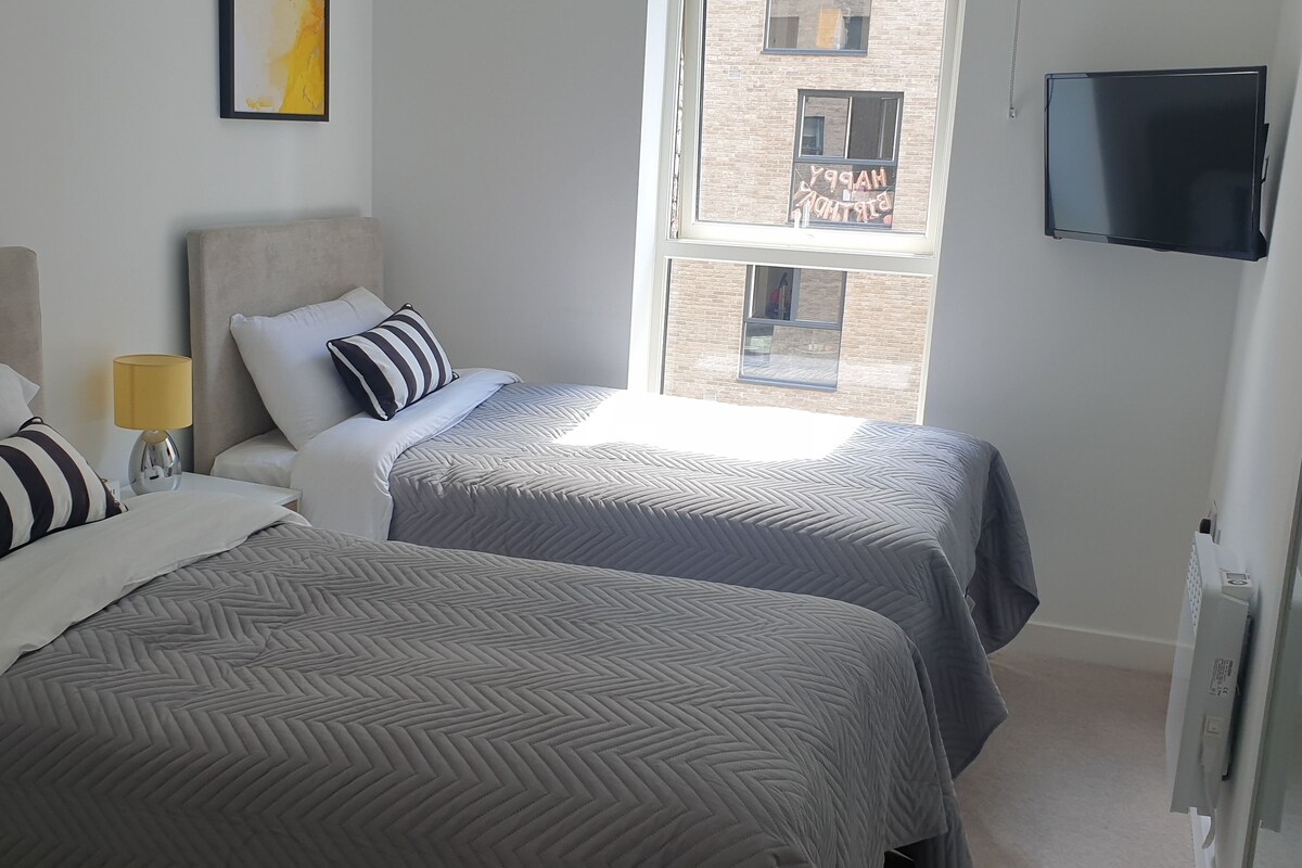 A hotel room with two beds, a TV, and a window with a view of a building.