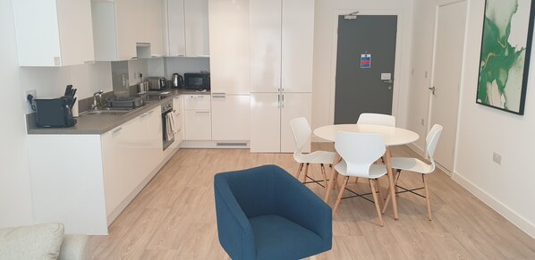 A modern kitchen with white cabinets, a dining table with chairs, and a blue sofa. - Quay Apartments Exchange Quay (Salford)