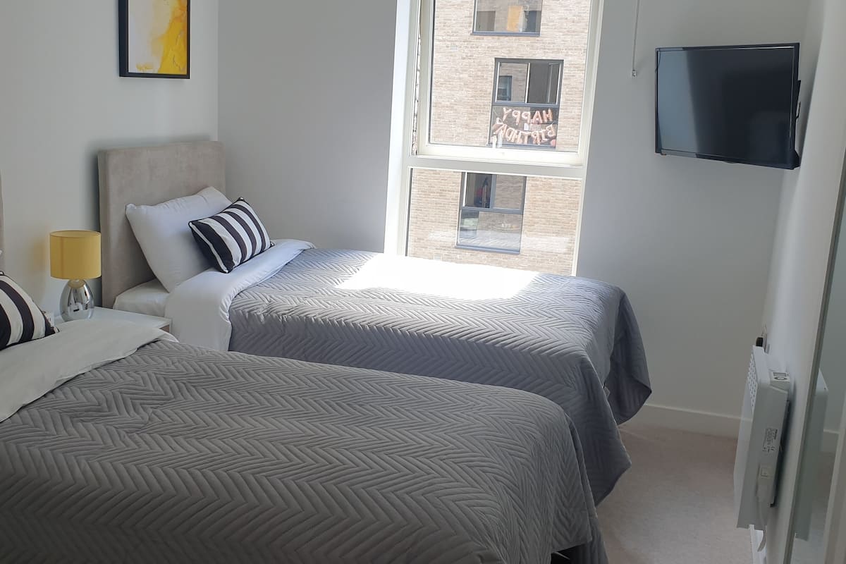 Ett hotellrum med två sängar, en tv och ett fönster med utsikt över en byggnad.